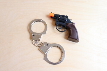 A pair of handcuffs with a fake revolver on a wood background. Toys or cinema accessories...