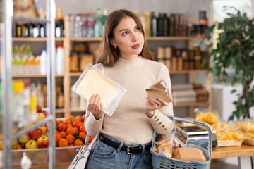 Young woman buyer chooses fresh cheese in grocery store