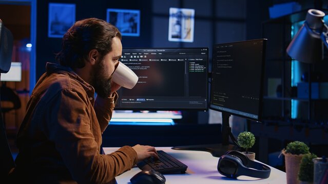 Stressed engineer feeling pressed by deadline, thinking how to finish developing code on PC. IT specialist brainstorming ways of solving database errors, working hard, drinking coffee, camera B