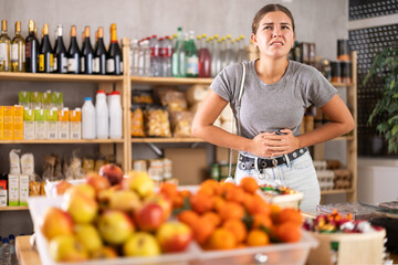 Young woman suffers from abdominal pain, feels pain in her stomach, while visiting a grocery supermarket