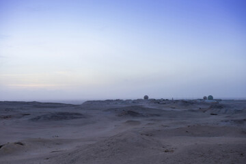 Vast desert landscape at dusk with remote structures and expansive horizon