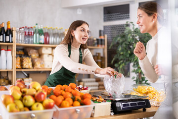 Helpful female vendor weighs candies on scales and sells candies to customer