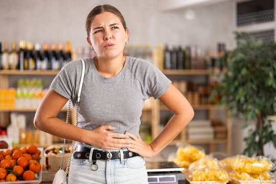 Young woman fidgeting by the stomach in the store. European woman felt unwell and indigestion in the supermarket.