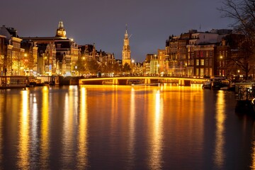 Fototapeta premium Canal in Amsterdam with illuminated buildings and reflection on the water