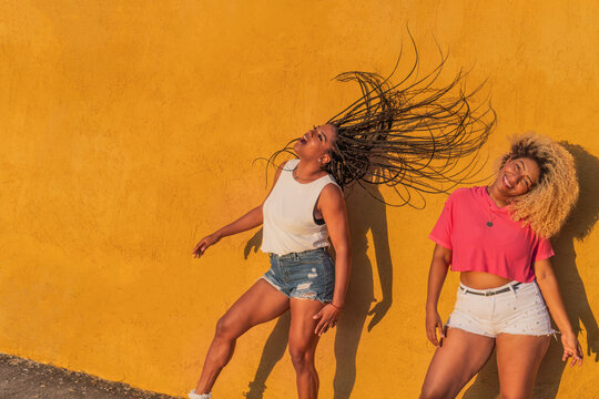 Two energetic women dancing and having fun against yellow wall