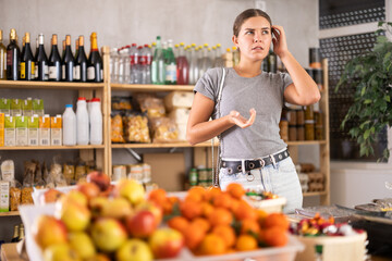 Puzzled woman forgot what she wanted to buy from the groceries in the supermarket. Customer remembers a list of purchases and food