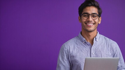 Confident young IT professional with glasses holding a laptop, standing against a vibrant purple background, symbolizing creativity and innovation.