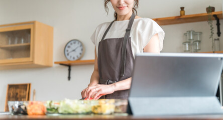 タブレットでアプリを使いレシピを見ながら料理するエプロン姿の女性  © buritora