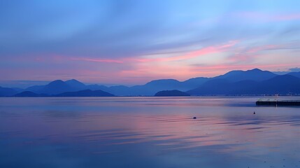 Fototapeta premium Serene twilight over calm waters with distant mountains and soft pastel skies.