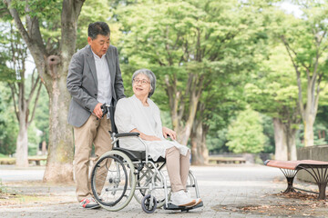 車椅子で公園を散歩するシニア・高齢者夫婦（介護）
