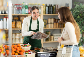 While working in store, seller answers customers questions about product, demonstrates sweets from stores assortment, opens packages with cookies and nougat and offers to get acquainted with products