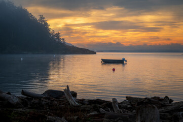 Small boat anchored in a quiet bay in the San Juan Islands during a beautiful sunset. The Salish Sea provides endless places to anchor out an explore remote islands and hidden bays and coves.