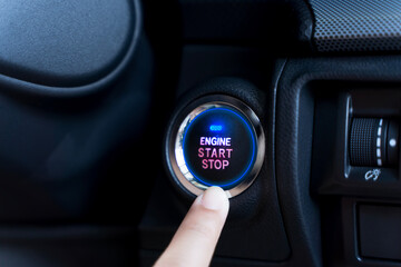 The driver palm as it presses the electric car engine start stop button with a blue light...