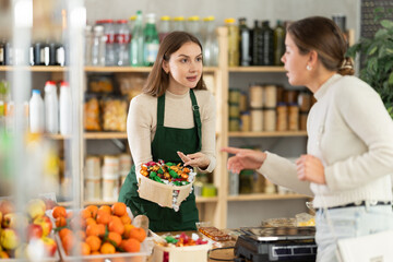 Female seller offers to buy candies to woman in interior of a grocery supermarket