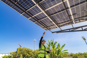 Engineer inspecting solar panels under a solar-powered carport on a sunny day, ensuring optimal...