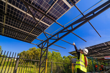 A female engineer in a safety vest and helmet inspecting a solar carport under construction. The...