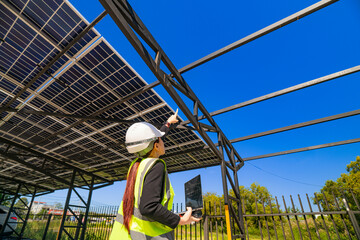 A female engineer in a safety vest and helmet inspecting a solar carport under construction. The...