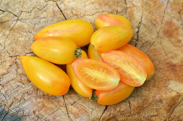 Group of ripe yellow tomatoes, belonging to the class of grape tomatoes, on an old tree stump as a background. Concept of growing varietal tomatoes.