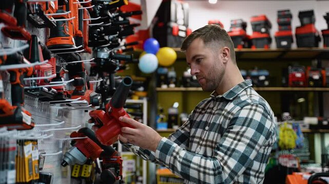 A man examines a red leaf blower displayed on a shelf in a hardware store
