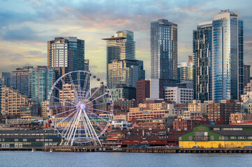 Seattle skyline with skyscrapers and a ferris wheel during a lovely sunset reflecting off the modern buildings.  View seen after the removal of the Alaskan Way Viaduct and a renovated waterfront.