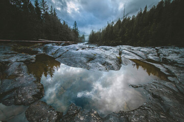 Tranquil Reflection of Cloudy Sky in a Rocky Forest Landscape. Foggy Mountain scene.