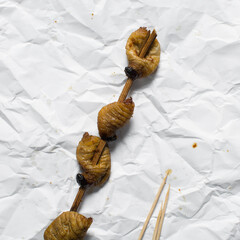 Overhead view of roasted sago worms on a white parchment paper, top view of palm worms on white...