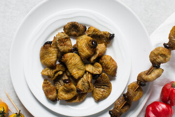 Overhead view of roasted sago worms on a white plate, top view of palm worms on marble background,...