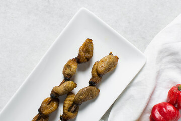 Overhead view of roasted sago worms on a white plate, top view of palm worms on marble background, roasted grub worms in a white dish