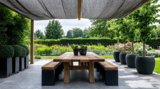 Wooden patio table with benches under shade sail in lush garden.