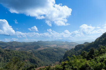 landscape of rolling green hills and valleys under a bright blue sky with scattered white clouds. Landmark hills of village Ban Jabo. Mae Hong Son of Thailand.