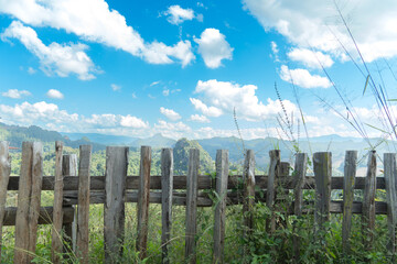 Fototapeta premium Wooden fence overlooks a scenic view of rolling hills. Under view of bright blue sky with fluffy white clouds. Traveling in Thailand of village Ban Jabo Mae Hong Son.