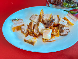 Fried crispy pork belly on white plate and red table.