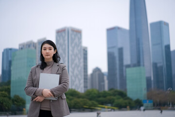 Confident Businesswoman Standing in Urban Skyline with Laptop