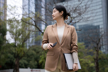 Confident Businesswoman in City Park with Smartphone and Notebook