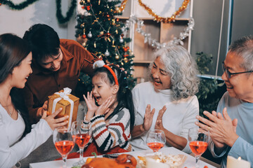 Portrait of Asian family exchanging presents during christmas at home. Attractive happy people holding gift box, celebrate holiday thanksgiving, xmas eve tradition in living room in house together.
