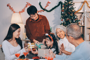 Portrait of Asian family exchanging presents during christmas at home. Attractive happy people holding gift box, celebrate holiday thanksgiving, xmas eve tradition in living room in house together.