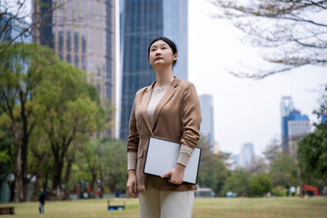 Fototapeta premium Empowered Businesswoman Reflecting Amidst Urban Skyscrapers in a Park