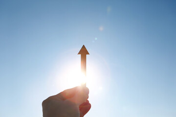 Hands holding up a rising arrow towards the sunrise sun, stock finance economy industry growth investment goal success concept
