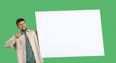 Young bearded man pointing at blank poster on green background