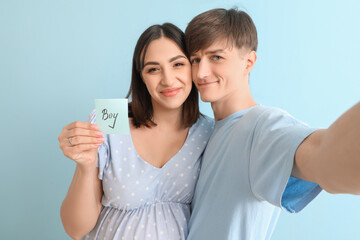 Young pregnant couple holding paper with word BOY on blue background