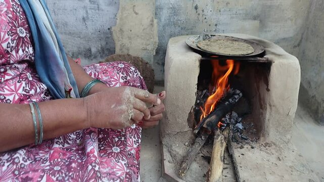 Indian woman cooking bajre ki roti on a traditional clay chulha, showcasing rural lifestyle and traditional cooking methods.