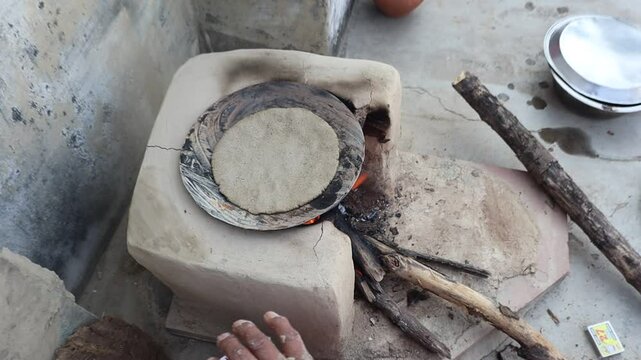 Indian woman cooking bajre ki roti on a traditional clay chulha, showcasing rural lifestyle and traditional cooking methods.