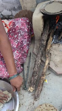 Indian woman cooking bajre ki roti on a traditional clay chulha, showcasing rural lifestyle and traditional cooking methods.