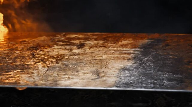 Camera glides across an oxidized metal surface with heat waves, against a dark background, creating an industrial atmosphere