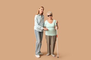 Young woman with blind grandmother on beige background