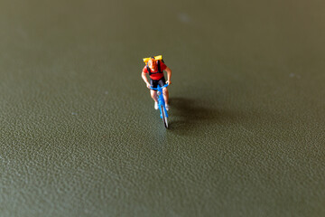 Close-up shot of a figurine of a cyclist riding a blue bicycle with a backpack