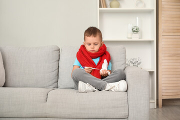 Sick little boy with thermometer and tissue sitting on sofa at home