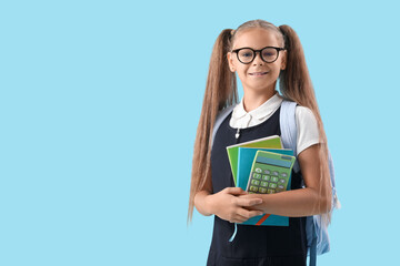 Cute little girl in school uniform with books and calculator on blue background