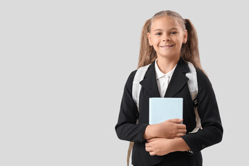 Naklejka premium Cute little girl in school uniform with book on grey background