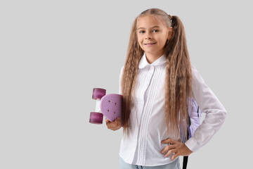 Cute little girl in school uniform with skateboard on grey background